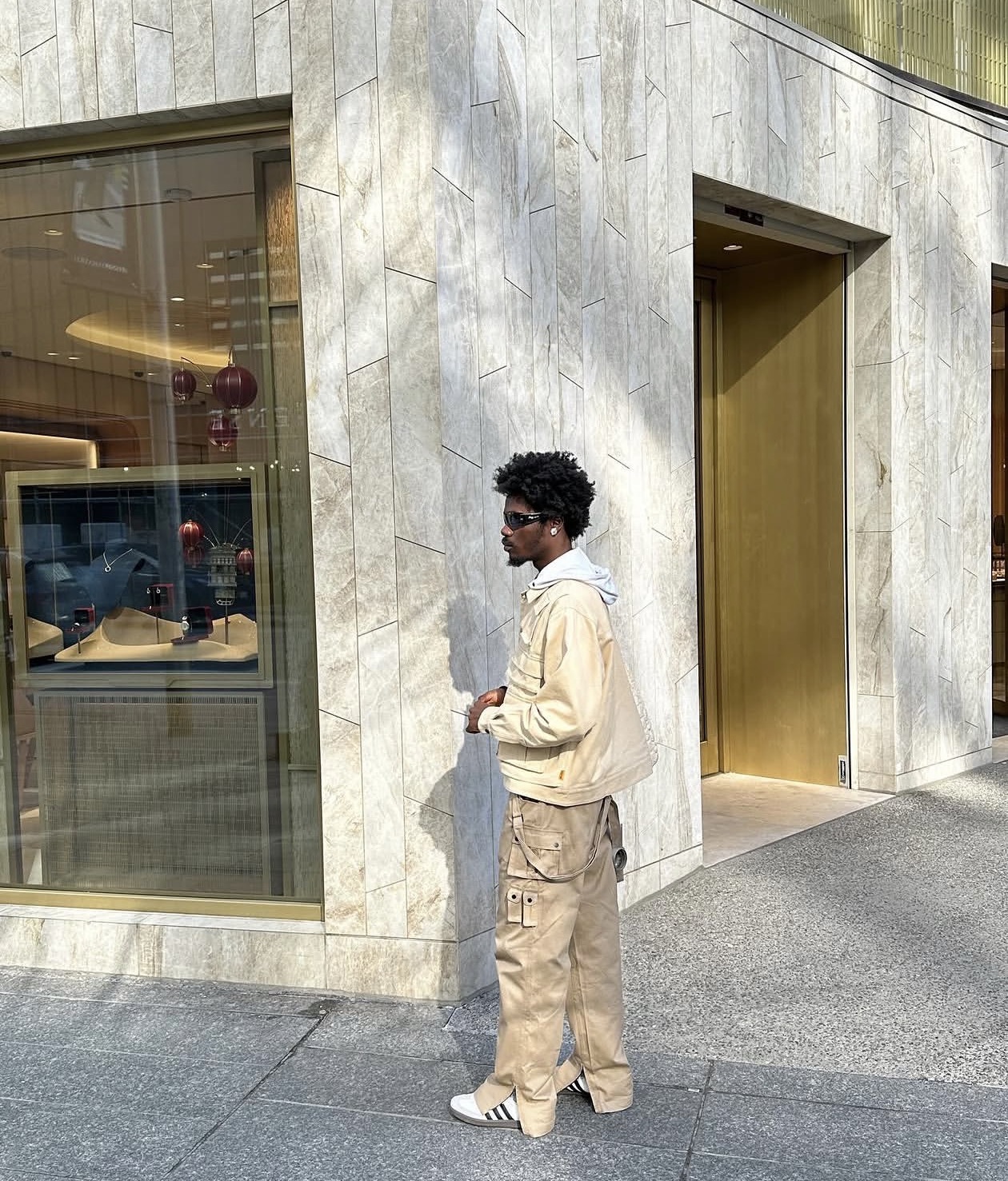 Editorial side profile — beige hooded jacket and cargo trousers in soft daylight